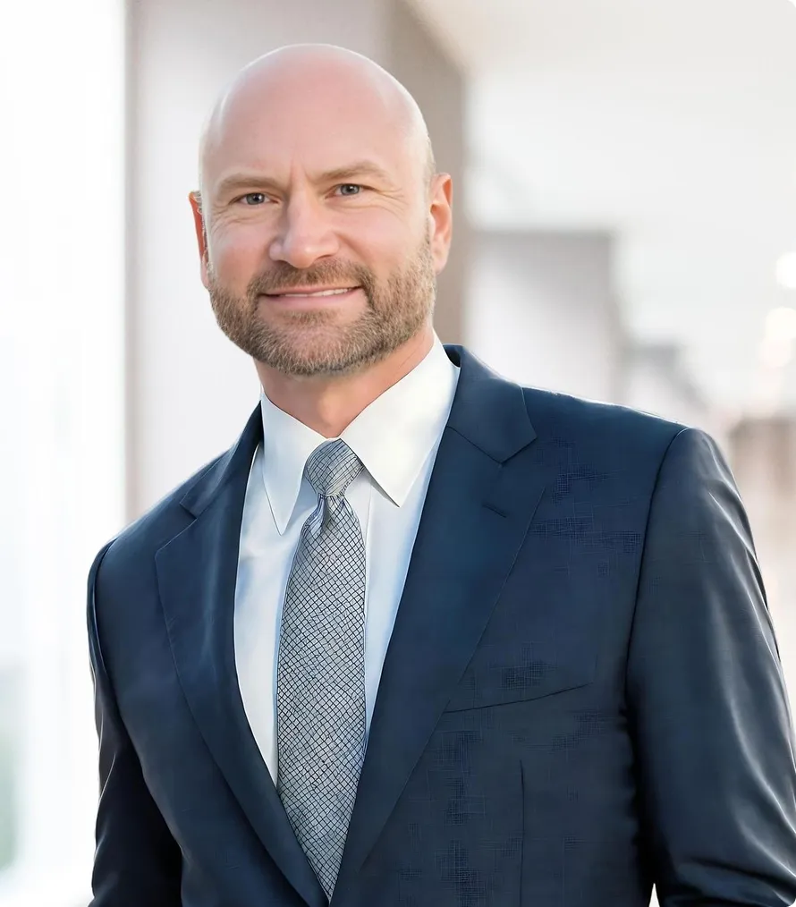 Professional middle-aged bald man with beard wearing dark blue suit and patterned tie.