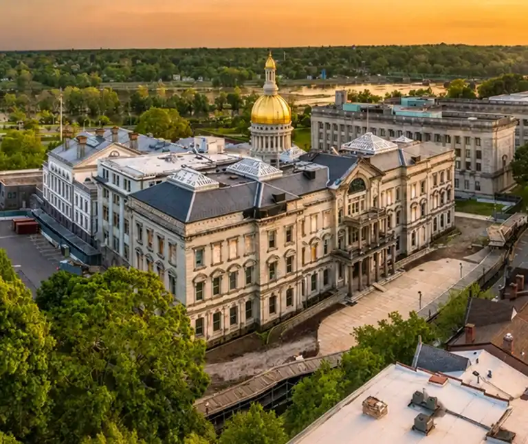 Aerial view of a historic government building with a golden dome at sunset, surrounded by trees and other structures.