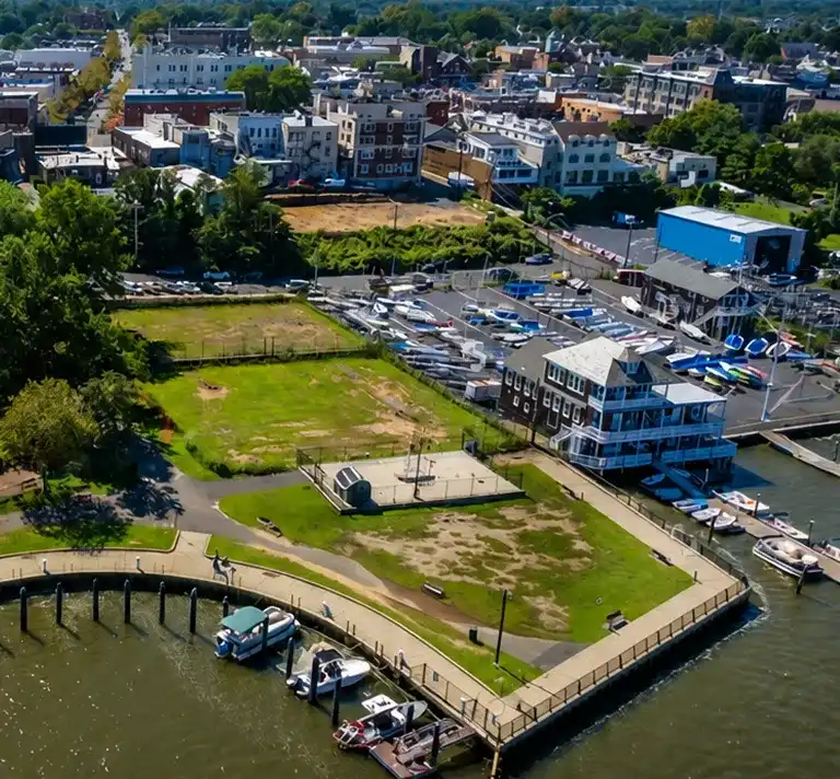 Aerial view of a waterfront park with boats docked, a marina, and residential buildings in the background.