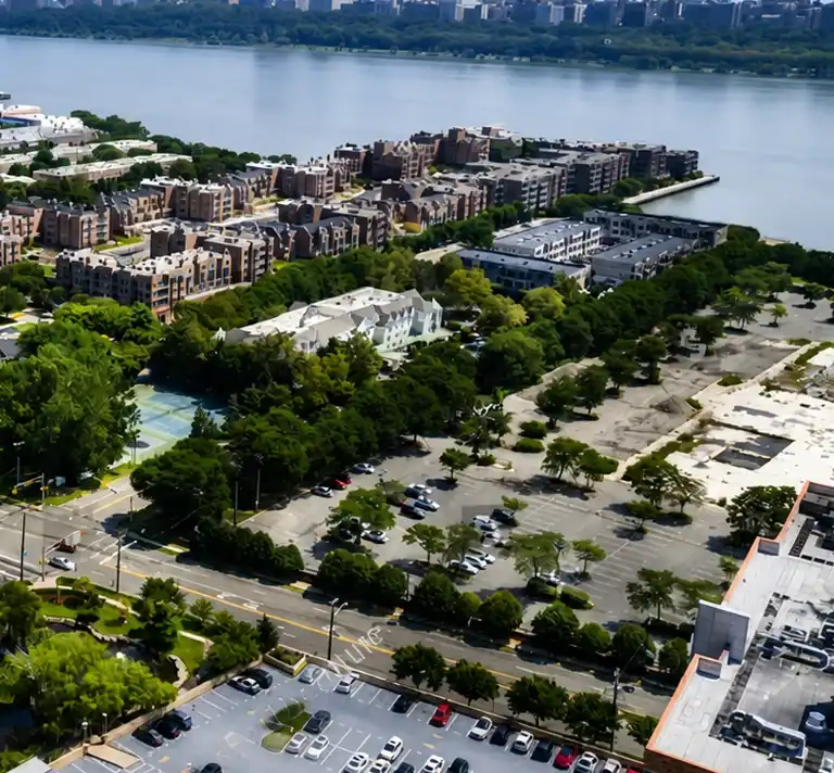 Aerial view of a waterfront urban area with residential buildings, green trees, and parking lots.