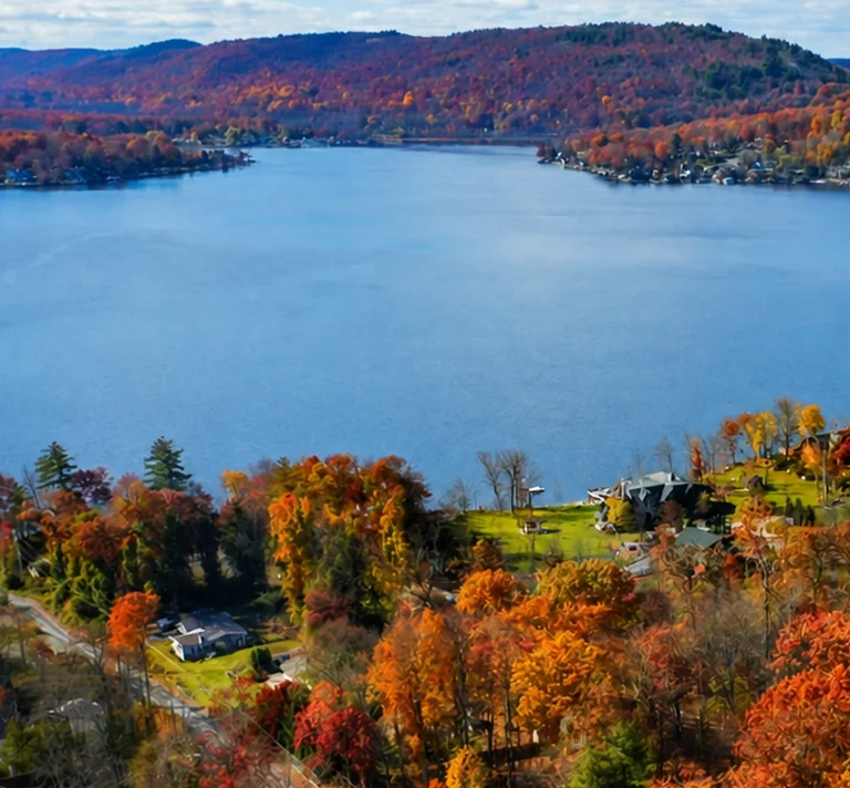 Aerial view of a lake surrounded by autumn-colored trees and residential houses.