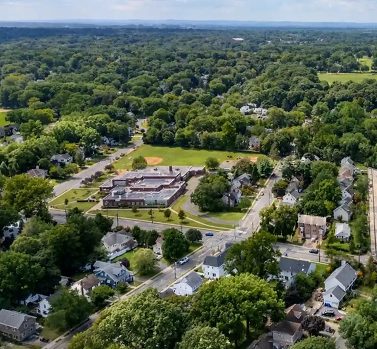 Aerial view of a suburban neighborhood with a central school building, surrounding houses, and abundant green trees.