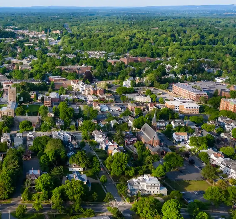 Aerial view of a suburban town with dense green trees, residential houses, and a prominent church.