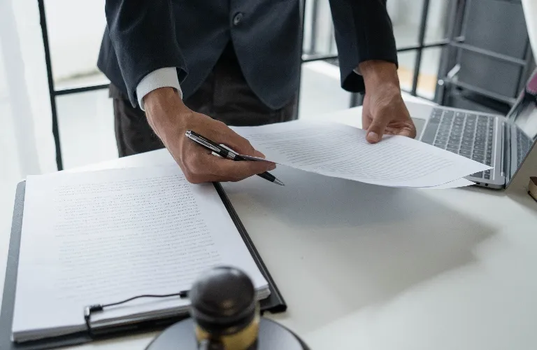 Person in dark suit reviewing documents on white desk with laptop and stamp.